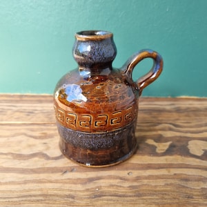 May include: A brown and blue ceramic pitcher with a geometric design. The pitcher has a handle and a spout.