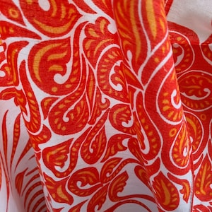 Puede incluir: Tela blanca con un patrón paisley rojo y naranja. La tela está doblada y el patrón es visible en ambos lados.
