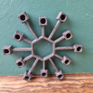 Op de afbeelding: Een zilveren metalen kandelaar met 12 kaarshouders die in een stervormig patroon zijn gerangschikt. De kandelaar is gemaakt van een geometrisch ontwerp met een zeshoekig midden.