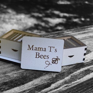 May include: A wooden box with a white lid that says "Mama T's Bees" with a bee illustration. The box is open and the lid is propped up.