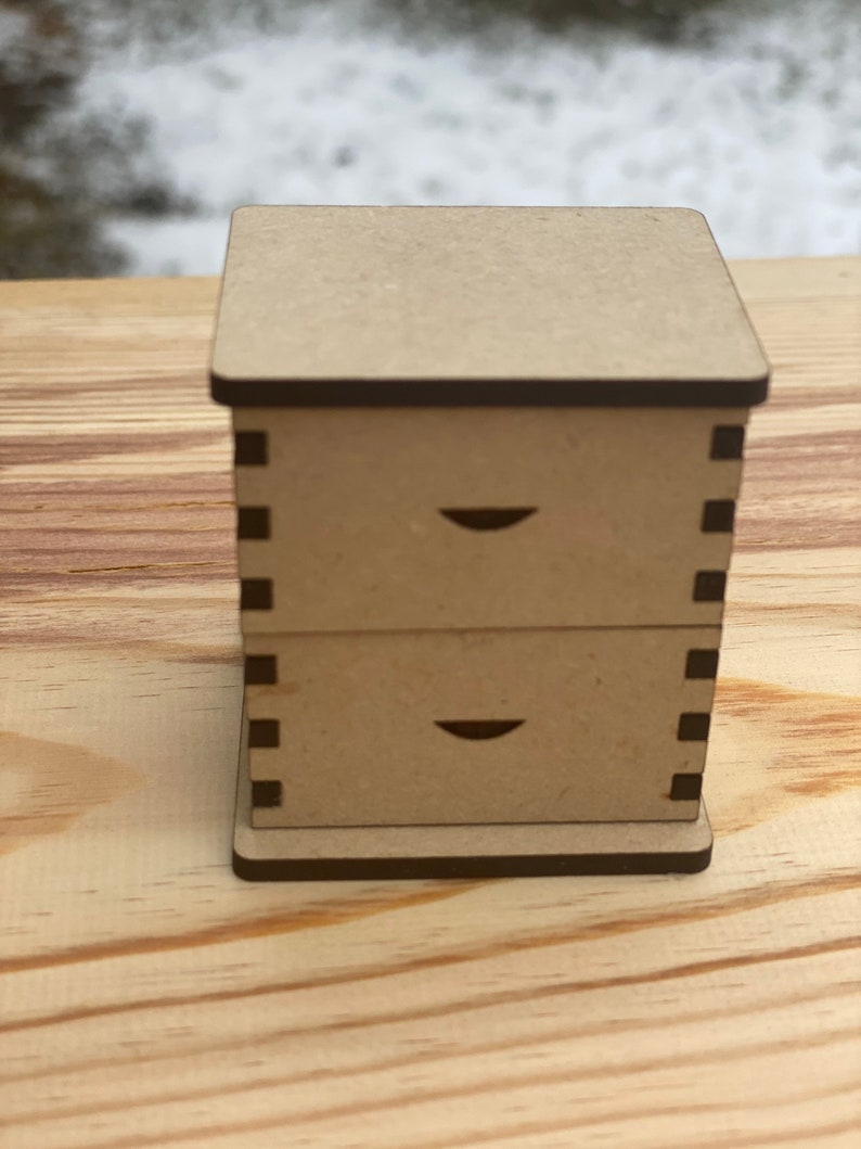 May include: A small wooden box with two drawers. The box is brown and has a black trim. The drawers have a small cutout on the front.