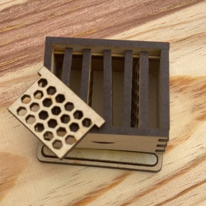 May include: A small wooden box with a honeycomb-shaped lid. The box is open and the lid is propped up. The box is made of light brown wood and has a dark brown stain.
