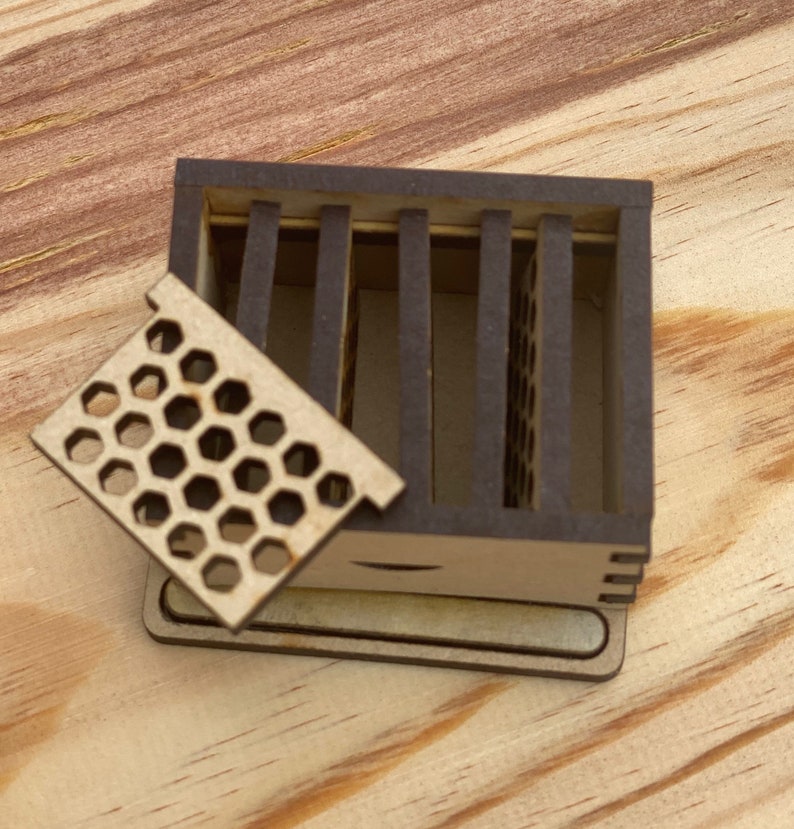 May include: A small wooden box with a honeycomb-shaped lid. The box is open and the lid is propped up. The box is made of light brown wood and has a dark brown stain.