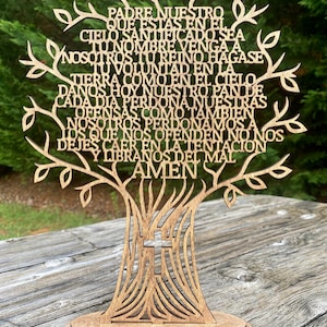 Puede incluir: Un &aacute;rbol de madera recortado con la oraci&oacute;n del Se&ntilde;or en espa&ntilde;ol, "Padre Nuestro", escrita en las ramas. El &aacute;rbol tiene una cruz en la base y se encuentra sobre una base de madera.