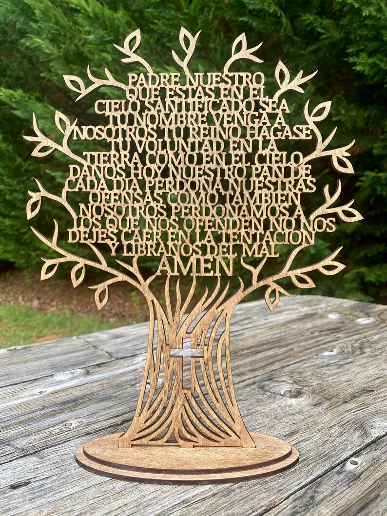 Puede incluir: Un &aacute;rbol de madera recortado con la oraci&oacute;n del Se&ntilde;or en espa&ntilde;ol, "Padre Nuestro", escrita en las ramas. El &aacute;rbol tiene una cruz en la base y se encuentra sobre una base de madera.