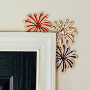 May include: Three wooden firework decorations in red, white, and blue, mounted on a white door frame.