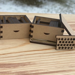 May include: Two small wooden boxes with a honeycomb design on the lid. The boxes are made of light brown wood and have a dark brown trim. The boxes are open and show the inside, which is also made of wood.