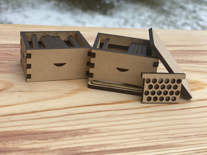 May include: Two small wooden boxes with a honeycomb design on the lid. The boxes are made of light brown wood and have a dark brown trim. The boxes are open and show the inside, which is also made of wood.
