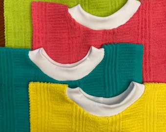 May include: Four colorful terry cloth bibs in shades of green, pink, teal, and yellow, each with a white ribbed collar. The bibs are arranged in a layered pattern, showcasing their soft texture and vibrant colors.