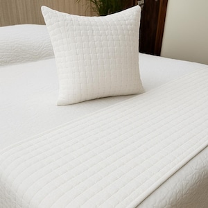 Pode incluir: Um conjunto de colcha e almofada acolchoadas brancas. A roupa de cama apresenta um padrão de grade e uma cor suave e neutra. A almofada é quadrada e colocada em cima da colcha. O tema geral é a decoração do quarto.