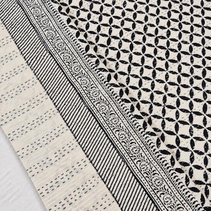 May include: A textile fabric featuring a cream-colored base with a black geometric pattern of interlocking circles. The border displays a detailed black floral vine motif alongside parallel diagonal lines and a section of horizontal dashed lines.