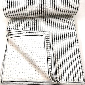 May include: A white and black striped quilt, partly rolled, with a black border. The quilt has vertical black stripes on a white background. Visible stitching adds texture. The design is simple and modern, suitable for a bed or sofa.