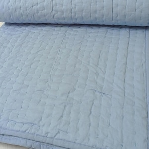 Puede incluir: Una colcha de color azul claro que presenta un patrón de cuadrícula con puntadas verticales y horizontales. La ropa de cama es de un color sólido con un borde acabado, mostrando una textura suave y un diseño acolchado uniforme.