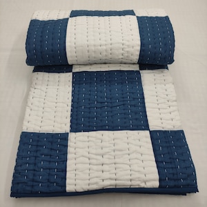 Könnte beinhalten: Eine gefaltete, gesteppte Decke mit einem Schachbrettmuster aus weißen und marineblauen Quadraten. Die Decke ist mit weißem Faden handgenäht, und der Stoff hat ein leicht strukturiertes Aussehen. Die Decke ist ordentlich gefaltet.