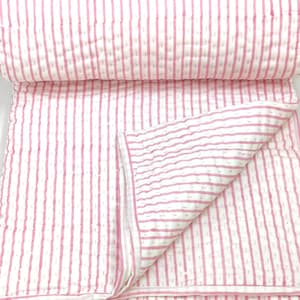 Op de afbeelding: Een gevouwen wit en roze gestreepte quilt. De quilt heeft verticale roze strepen op een witte achtergrond. De randen zijn afgewerkt met een roze rand. De quilt is opgevouwen en onthult het binnenpatroon.