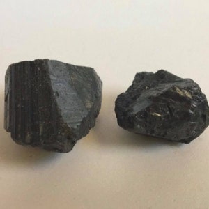 May include: Two black, rough, irregularly shaped stones. The stones are different sizes and have a matte finish.