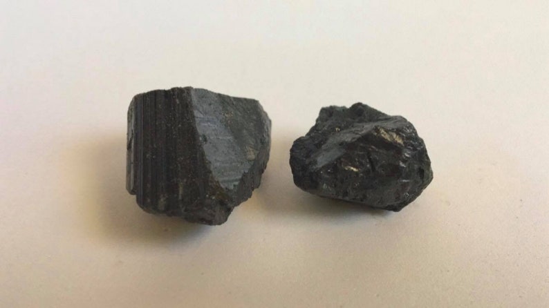May include: Two black, rough, irregularly shaped stones. The stones are different sizes and have a matte finish.