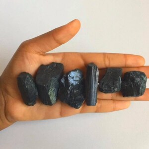 May include: A collection of black tourmaline crystals, some with a green sheen, in a hand. The crystals are various shapes and sizes.