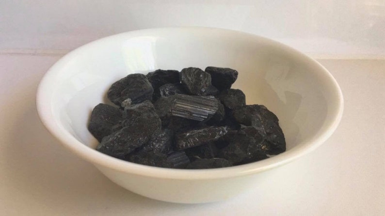 May include: A white bowl filled with black, rough, and irregularly shaped stones.