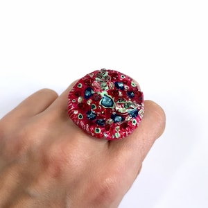 May include: A large, round, red ring with a colourful, abstract design. The ring is decorated with blue, green, and gold accents.