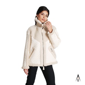 May include: A cream-colored, quilted jacket with a zipper closure and a brown buckle detail. The jacket has a faux fur lining and a chevron pattern on the front.