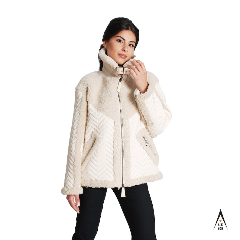May include: A cream-colored, quilted jacket with a zipper closure and a brown buckle detail. The jacket has a faux fur lining and a chevron pattern on the front.