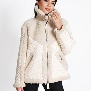 May include: A cream-colored, faux fur jacket with a quilted design. The jacket has a zipper closure and a buckle detail on the collar.
