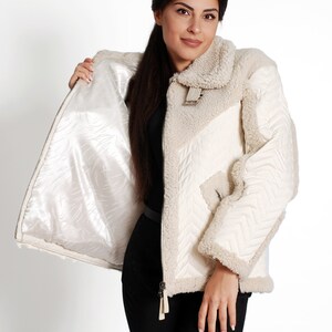May include: A white shearling jacket with a quilted lining and a zipper closure. The jacket has a stand-up collar and a flap pocket on the left side.