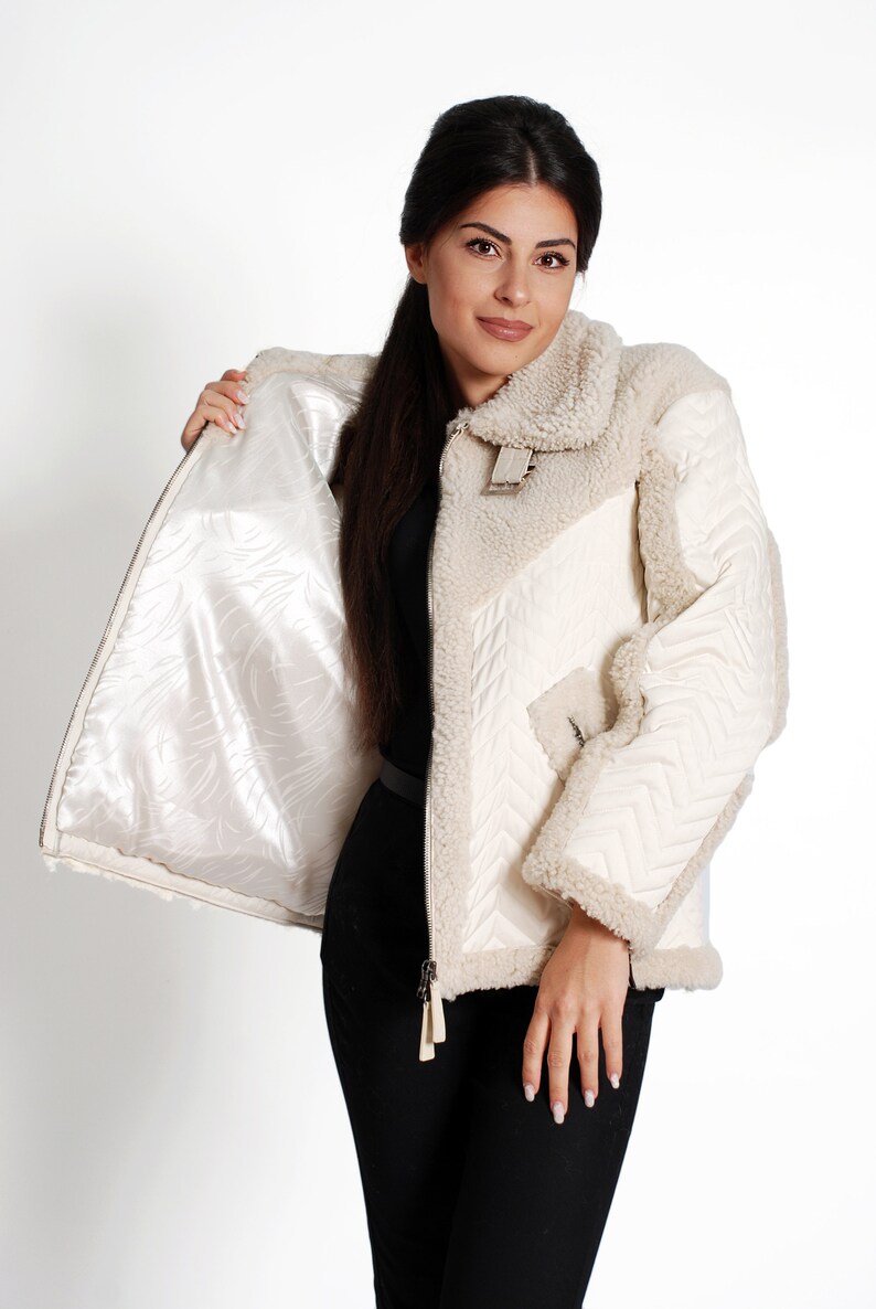 May include: A white shearling jacket with a quilted lining and a zipper closure. The jacket has a stand-up collar and a flap pocket on the left side.