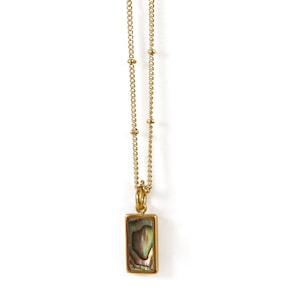 Puede incluir: Un collar de cadena dorada con un colgante rectangular con una concha de abulón iridiscente.