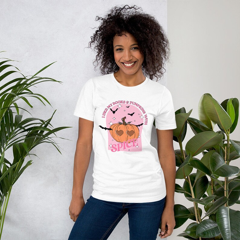 May include: White t-shirt with a pink graphic of a pumpkin with heart-shaped eyes and the text "I like my books & pumpkins with spice!"