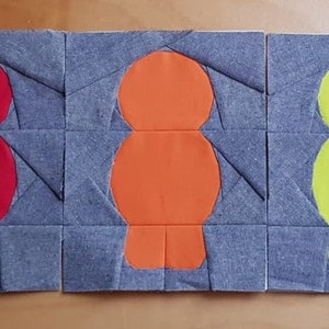 May include: A patchwork quilt with six bird-shaped appliqués in a row. The birds are in purple, red, orange, yellow, green, and blue, set against a grey background. The quilt is constructed from small, square fabric pieces.