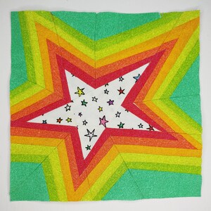May include: A colorful patchwork quilt block featuring a large white star with small stars printed on it. The star is surrounded by concentric rings of red, orange, yellow, and green fabric.