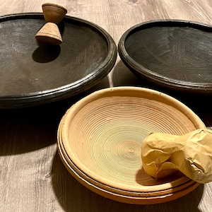 May include: A collection of handcrafted wooden bowls and a mortar and pestle set. The bowls are in various sizes and colors, including black and natural wood tones. The mortar and pestle are made of wood.