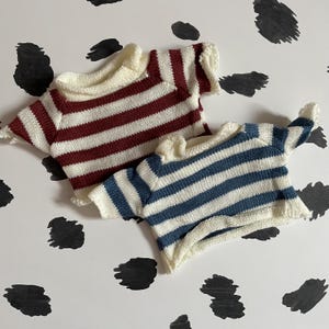 May include: Two striped knitted shirts, one with red and white stripes and one with blue and white stripes.