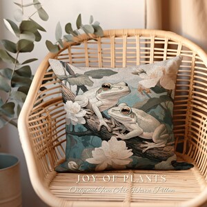May include: A decorative throw pillow with a blue and green floral design featuring two white frogs. The pillow has the text "JOY OF PLANTS Original Fine Art Woven Pillow" printed on the bottom.