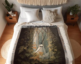Puede incluir: Una manta tejida que muestra una figura de fantasma de pie en un jardín oscuro y cubierto de vegetación con arcos de piedra y hojas de otoño. La manta tiene un borde con flecos y está colocada sobre una cama con almohadas blancas.