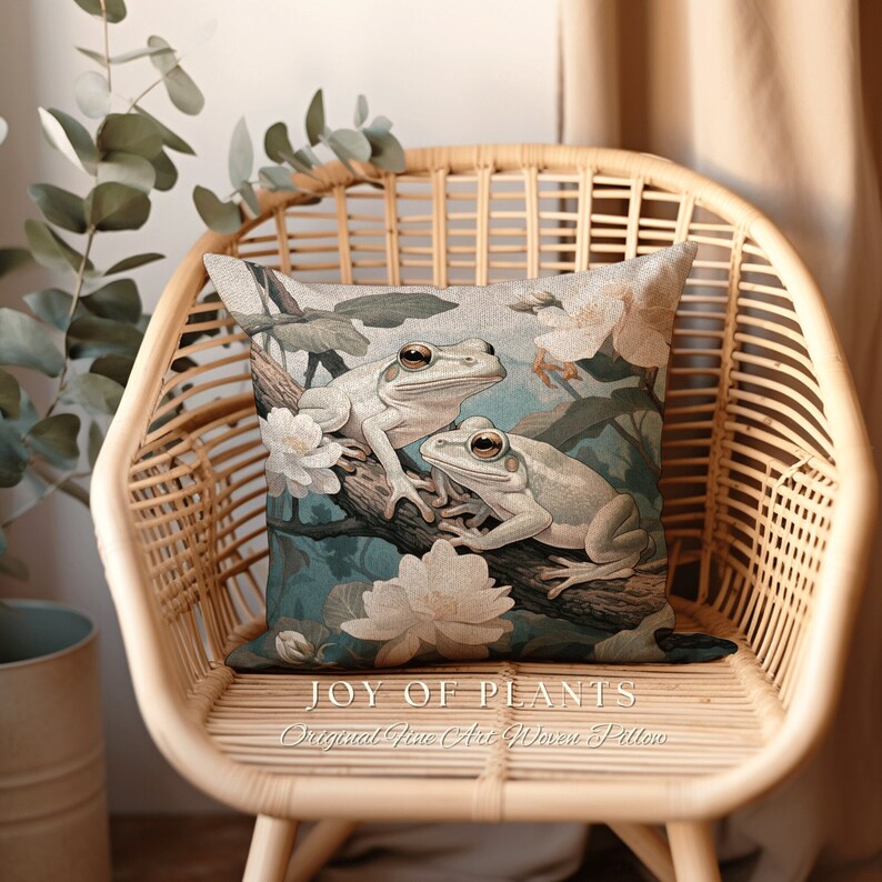 May include: A decorative throw pillow with a blue and green floral design featuring two white frogs. The pillow has the text "JOY OF PLANTS Original Fine Art Woven Pillow" printed on the bottom.
