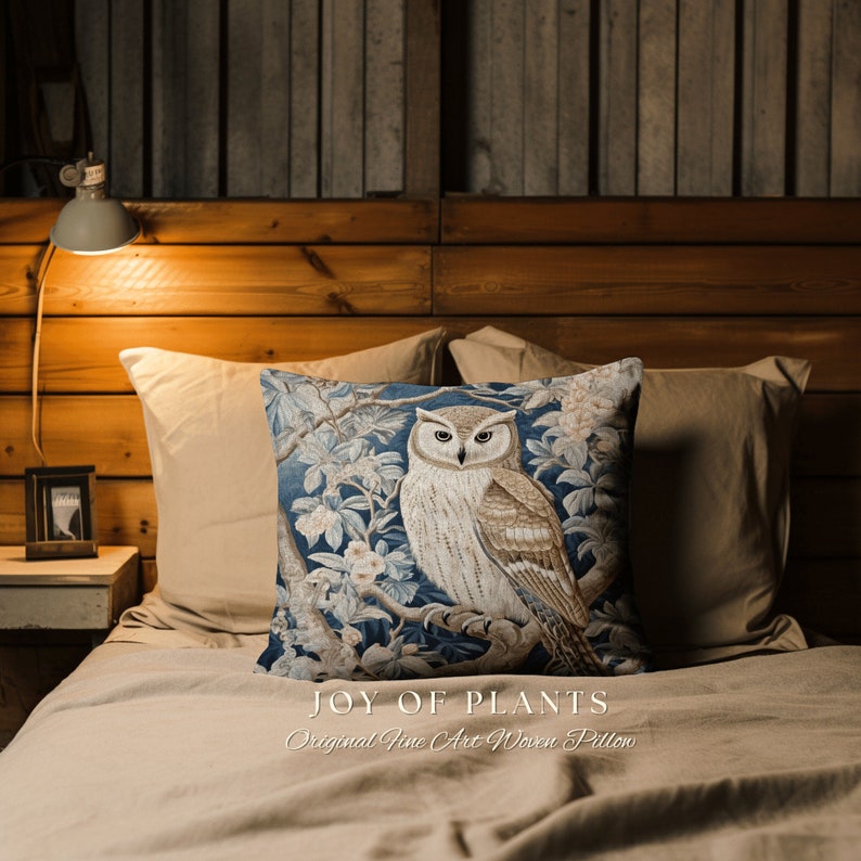May include: A decorative throw pillow with a woven design of an owl perched on a branch with flowers. The pillow is blue, brown, and white and has the text "JOY OF PLANTS Original Fine Art Woven Pillow" printed on the bottom.