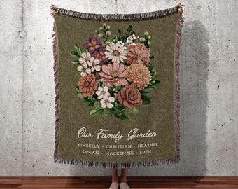 May include: Olive green throw blanket featuring a floral bouquet in pink, peach, and white. The text "Our Family Garden" and names are printed below the flowers. The blanket has a fringed edge and the text "JOY OF PLANTS" is at the bottom.