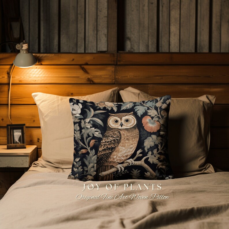 Op de afbeelding: Een decoratief kussen met een tapijt-achtig ontwerp met een uil die op een tak zit, omringd door bloemen en bladeren. Het kussen heeft een donkerblauwe achtergrond met bruine, beige en roze accenten. De tekst "JOY OF PLANTS Original Fine Art Woven Pillow" is onder de afbeelding gedrukt.
