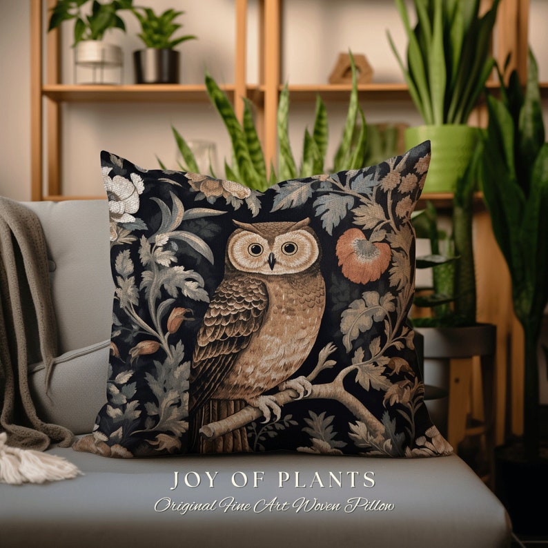 Op de afbeelding: Een decoratief kussen met een zwarte achtergrond waarop een bruine uil op een tak zit, omringd door ingewikkelde bloemmotieven. Het kussen heeft de tekst "JOY OF PLANTS Original Fine Art Woven Pillow" onderaan gedrukt.
