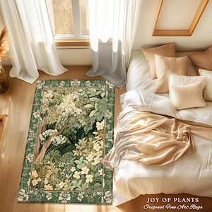 May include: A rectangular green rug with a floral and tree design. The rug features a border of flowers and a central image of a tree with white flowers and green leaves. The text "JOY OF PLANTS Original Fine Art Rugs" is in the bottom right corner.