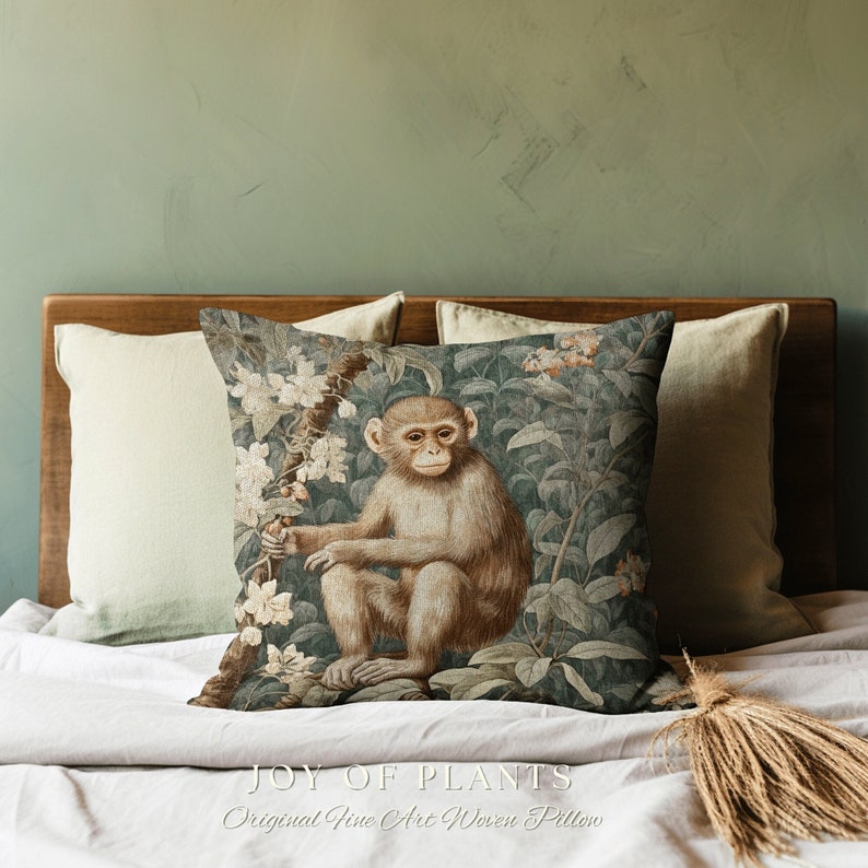 Pode incluir: Uma almofada decorativa com um design tecido que apresenta um macaco sentado em um ambiente exuberante de selva verde. A almofada tem um fundo marrom com folhas verdes e flores brancas. O macaco &eacute; marrom com o rosto branco e est&aacute; sentado em um galho. O texto "JOY OF PLANTS Original Fine Art Woven Pillow" est&aacute; impresso na parte inferior da almofada.