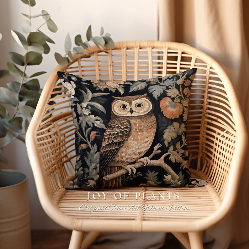 Op de afbeelding: Een kussen met een donkere achtergrond met een gedetailleerd tapijtontwerp van een uil die op een tak zit met bloemen en bladeren. De tekst "JOY OF PLANTS Original Fine Art Woven Pillow" is onder het kussen gedrukt.