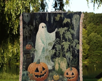 Puede incluir: Una manta de tapiz tejida que presenta una escena de Halloween con un fantasma, calabazas y follaje. La manta tiene un fondo oscuro con un fantasma azul claro y calabazas naranjas. El texto "JOY OF PLANTS Original Fine Art Throws" está en la parte inferior.