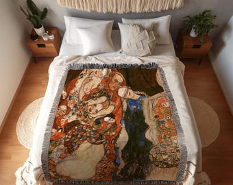 Puede incluir: Una manta tejida con una reproducción de una pintura de Gustav Klimt, con figuras en tonos cálidos de naranja, rojo y dorado, acentuadas por azul y verde. La manta tiene flecos y se muestra sobre una cama con ropa de cama blanca. El texto "JOY OF PLANTS SHOP" y "Custom Fine Art Blankets" es visible.