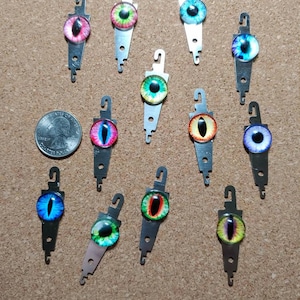 May include: Twelve colorful eye-shaped threaders with metal hooks. The threaders are arranged in a semi-circle on a brown corkboard.