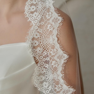 May include: White bridal veil with a delicate lace trim. The lace features a floral pattern with a scalloped edge.