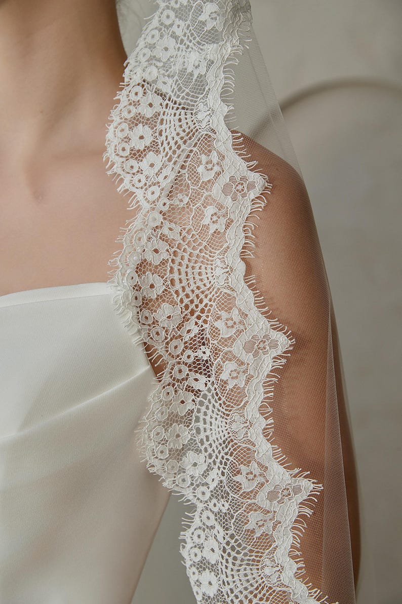 May include: White bridal veil with a delicate lace trim. The lace features a floral pattern with a scalloped edge.